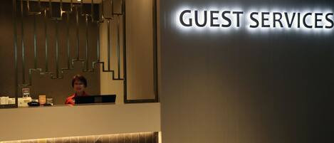 Ein Empfangstresen mit einem Schild, das "GUEST SERVICES" zeigt, und einem modernen Innendesign.