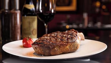 A steak on a plate with a glass of red wine and a bottle of wine in the background.