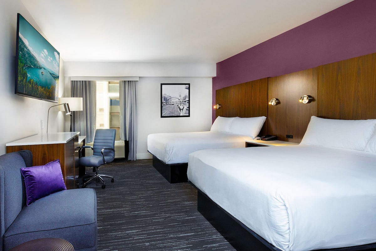 A hotel room with two beds, a desk, a chair, a TV, and a painting.