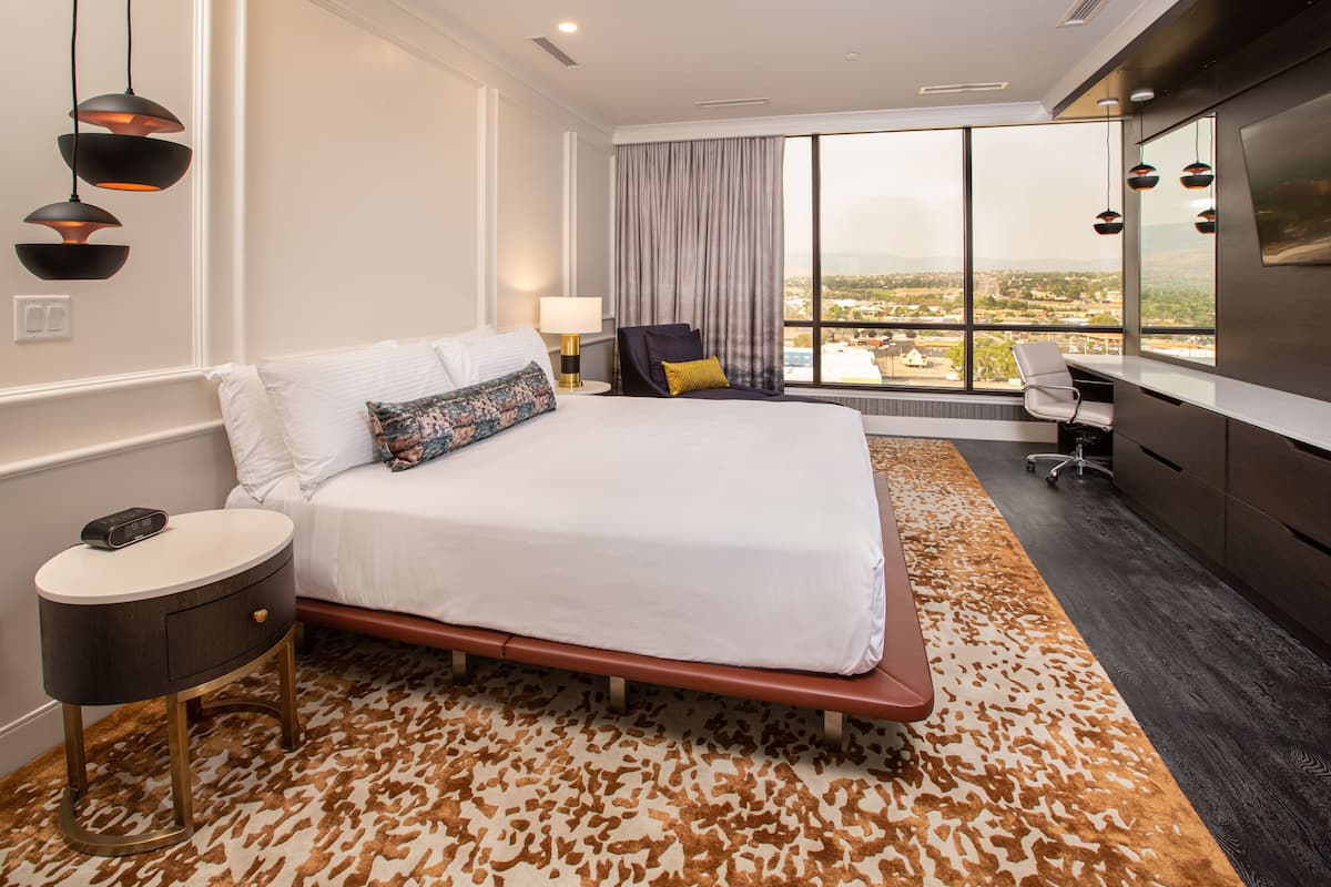 A hotel room with a large bed, a desk, a chair, and a view of the city.