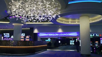 Un área de estar moderna con un cartel llamativo de 'AfterGlow Lounge', un techo decorativo con elementos colgantes y un suelo alfombrado con un diseño.