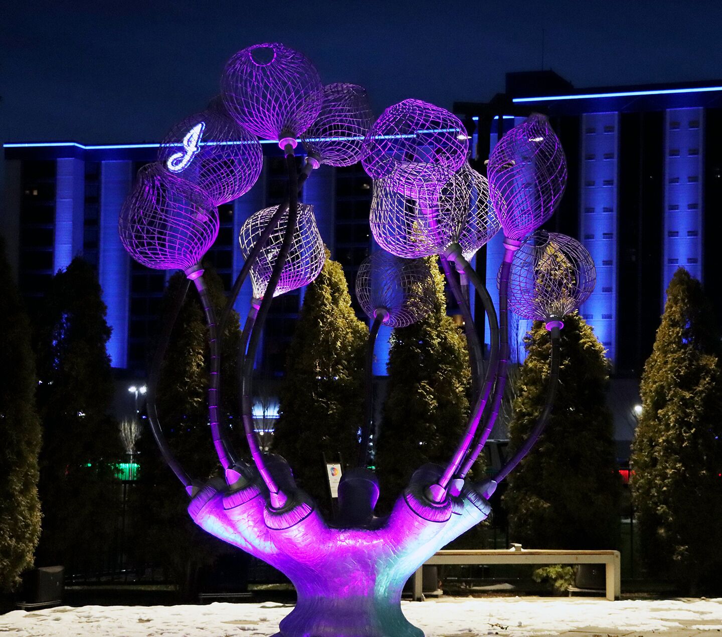 A sculpture with multiple spherical elements and a central base, set against a backdrop of buildings and trees.