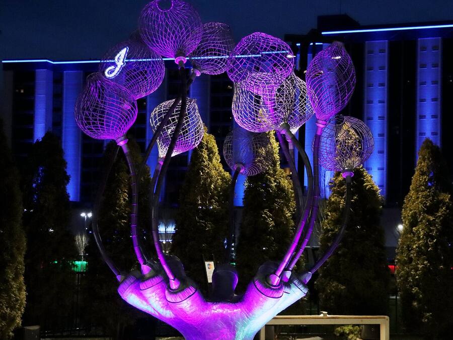 Una escultura con varios elementos esféricos y una base central, frente a un fondo de edificios y árboles.