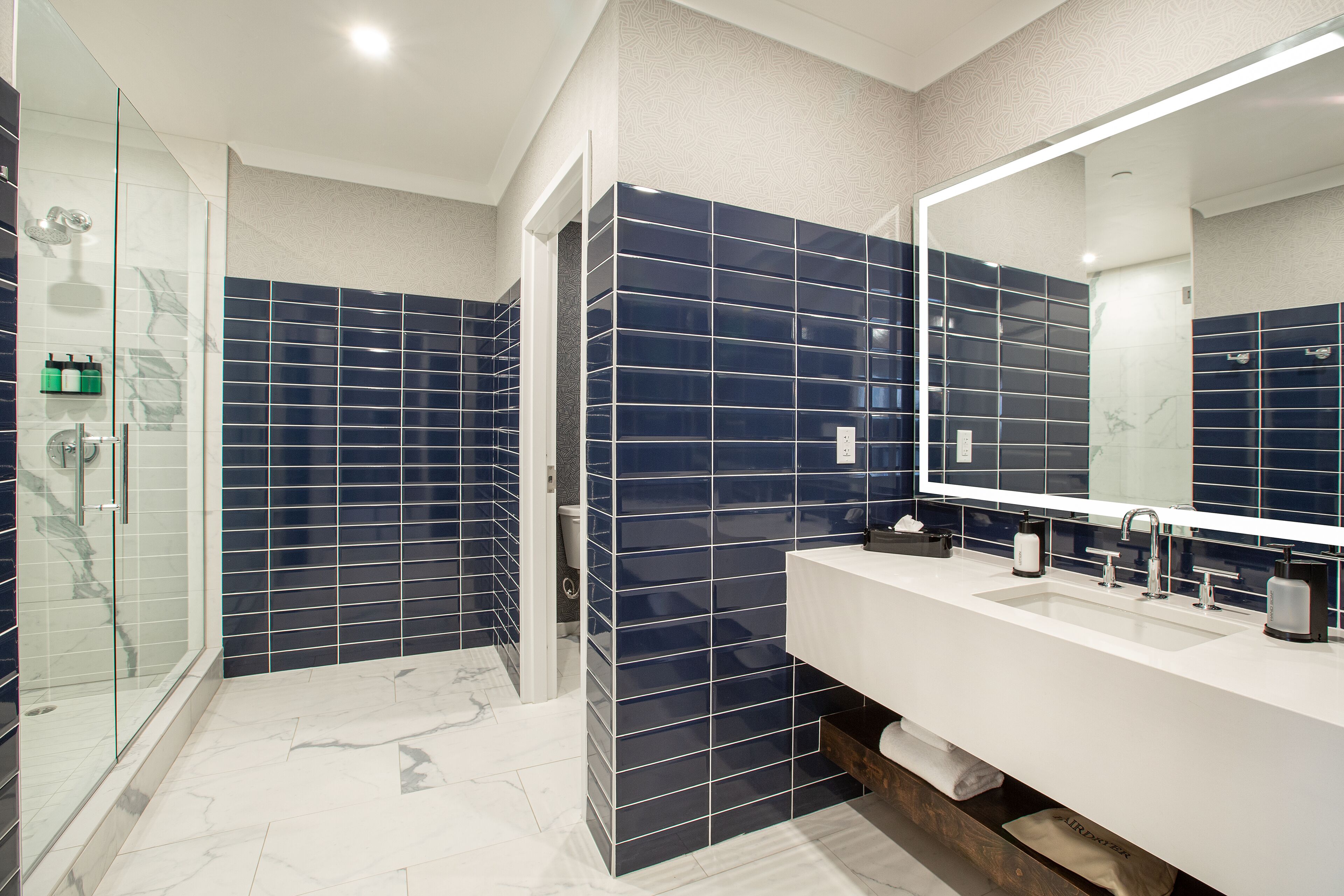 A modern bathroom with a glass shower enclosure, a double sink vanity, and dark blue tiled walls.