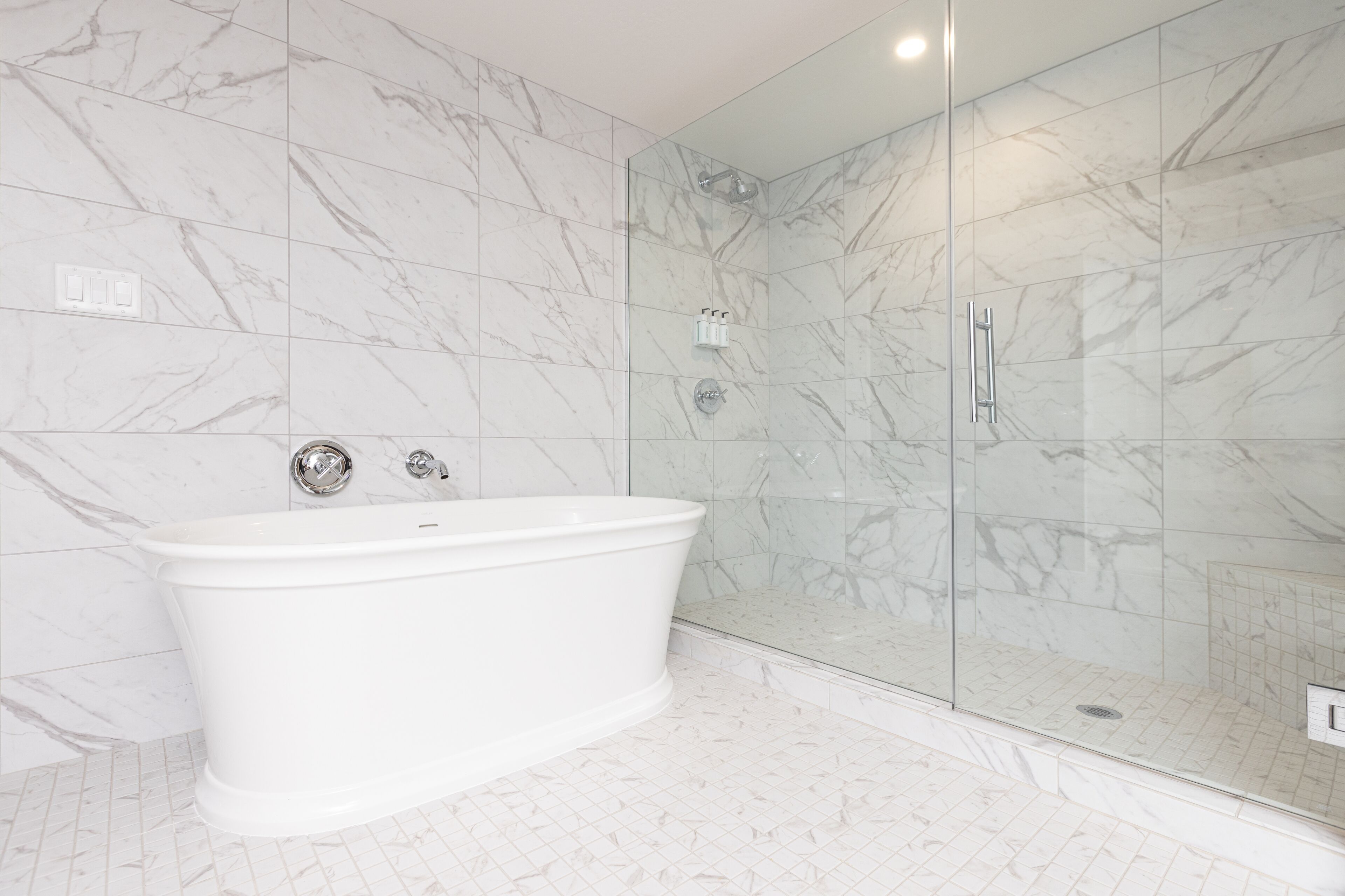 A bathroom with a freestanding bathtub, a glass-enclosed shower, and marble walls.