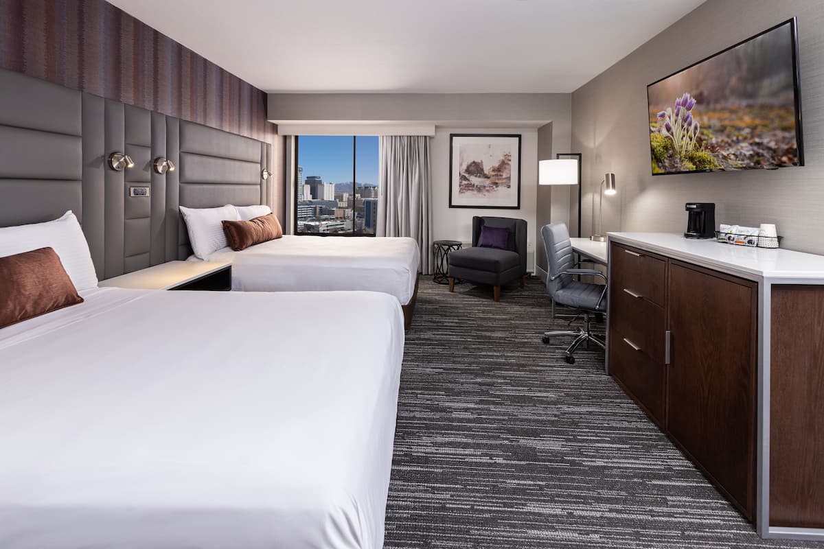 A hotel room with two beds, a desk, a chair, a coffee maker, and a city view.