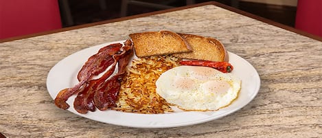 A plate with bacon, toast, fried egg, and hash browns on a marble table.
