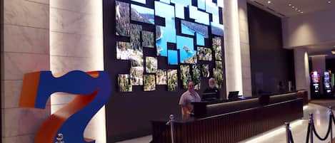A hotel reception area with a large '7' sign, a modern reception desk, and a wall of framed photographs.