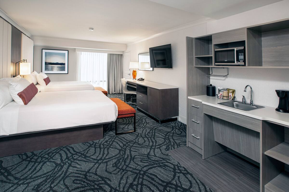 Une chambre d’hôtel avec deux lits, un bureau, un four à micro-ondes, un lavabo et une grande fenêtre donnant sur un beau paysage.