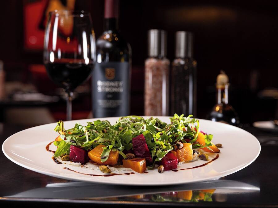 A plate of food with various vegetables and a bottle of wine in the background.