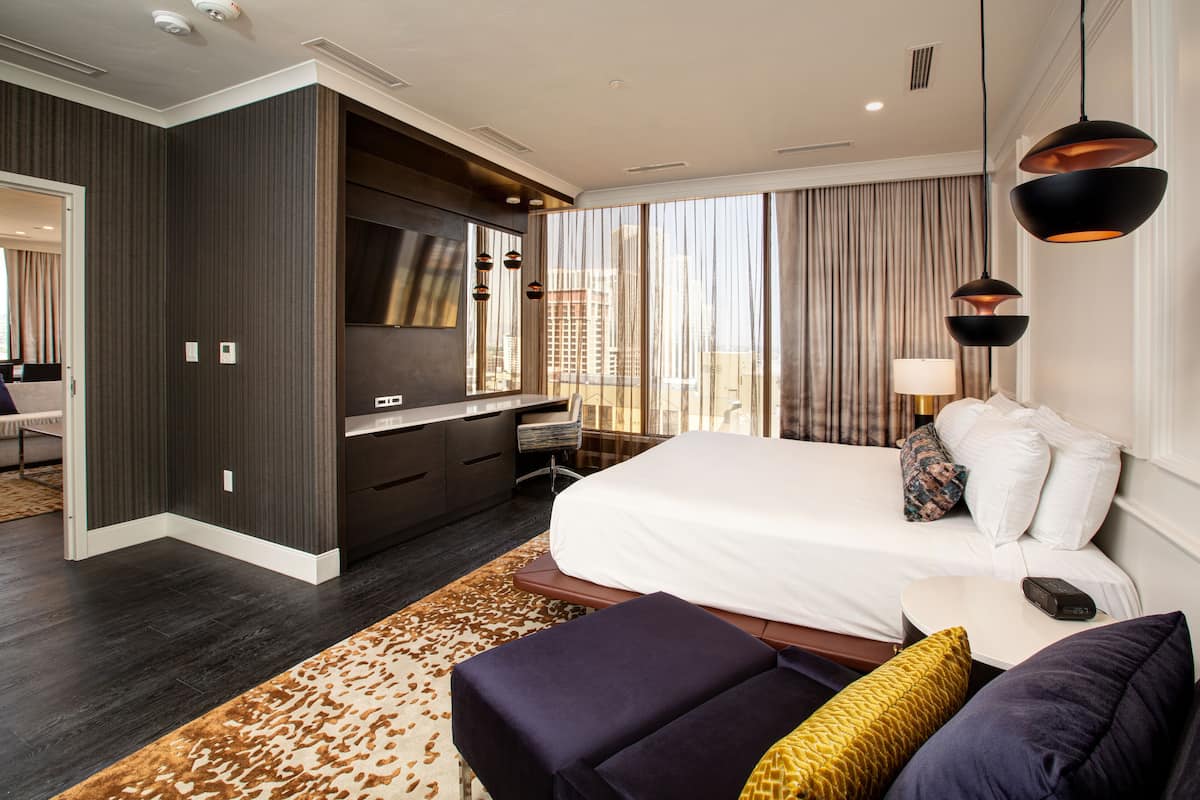 A modern hotel room with a large bed, a desk, and a view of the city.