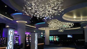 A modern lobby with a high ceiling, illuminated by a chandelier and neon lights. There are gaming machines and a reception desk with illuminated letters. - J Resort (Reno)
