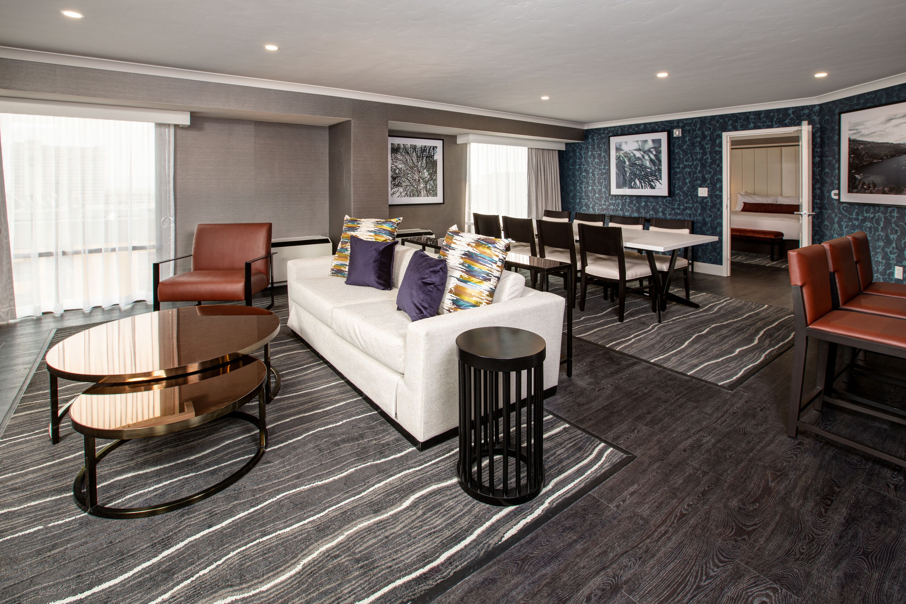 A modern hotel room with a sofa, armchairs, a dining table, and a small coffee table.