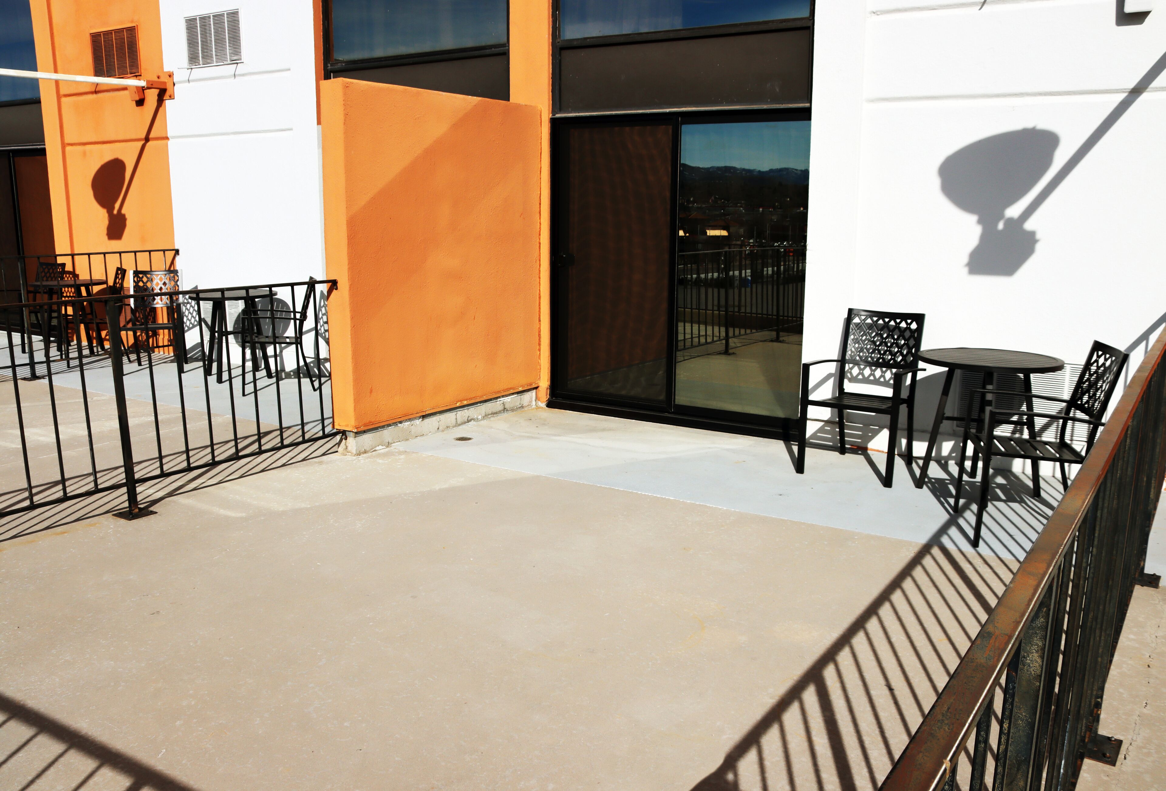 An outdoor terrace with a concrete floor, black metal railings, and a seating area with tables and chairs.