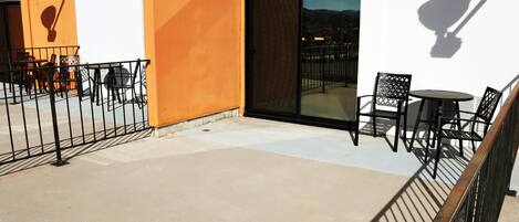 An outdoor terrace with a concrete floor, black metal railings, and a seating area with tables and chairs.