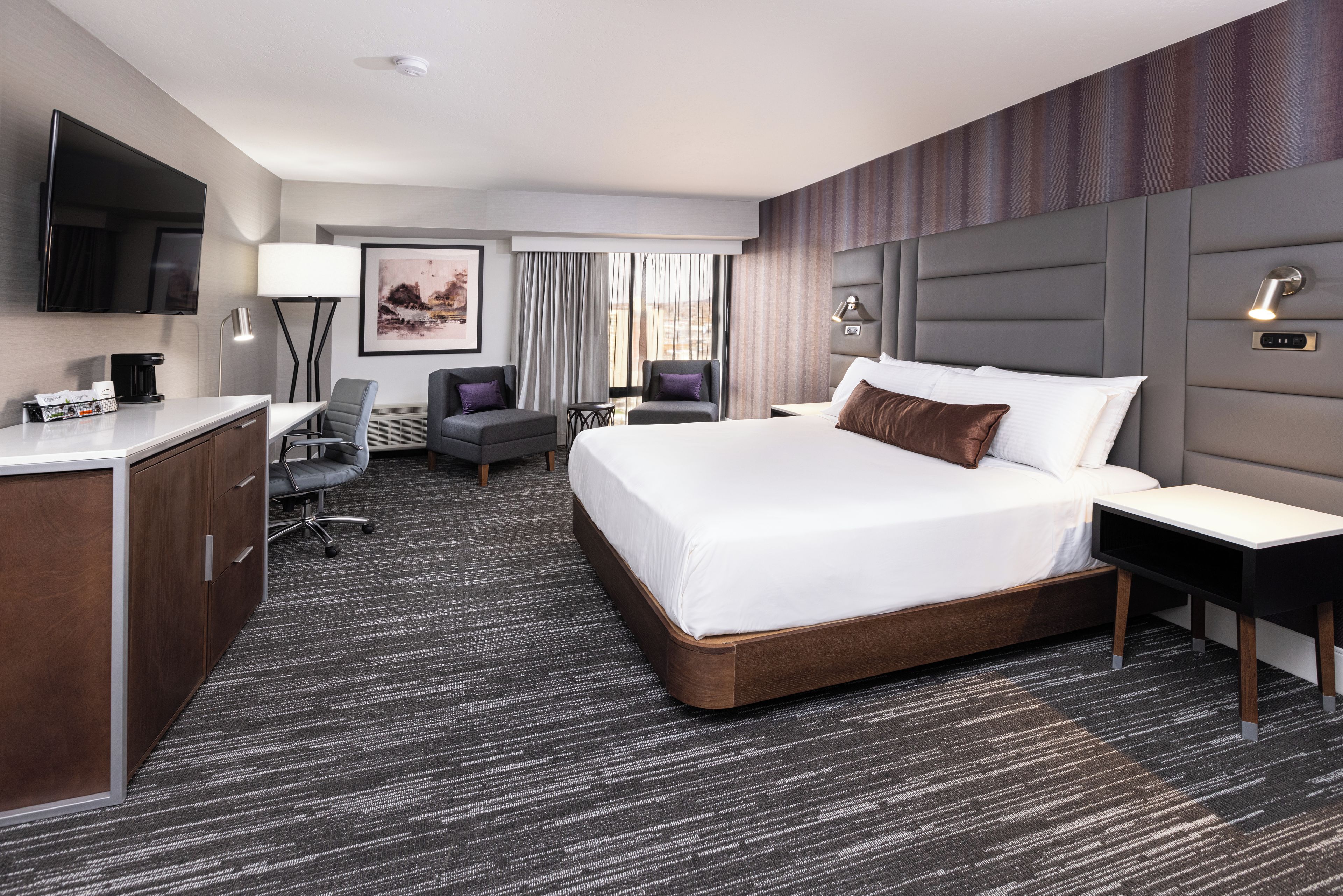 Een hotelkamer met een groot bed, een bureau, een stoel, een televisie en een raam met gordijnen.
