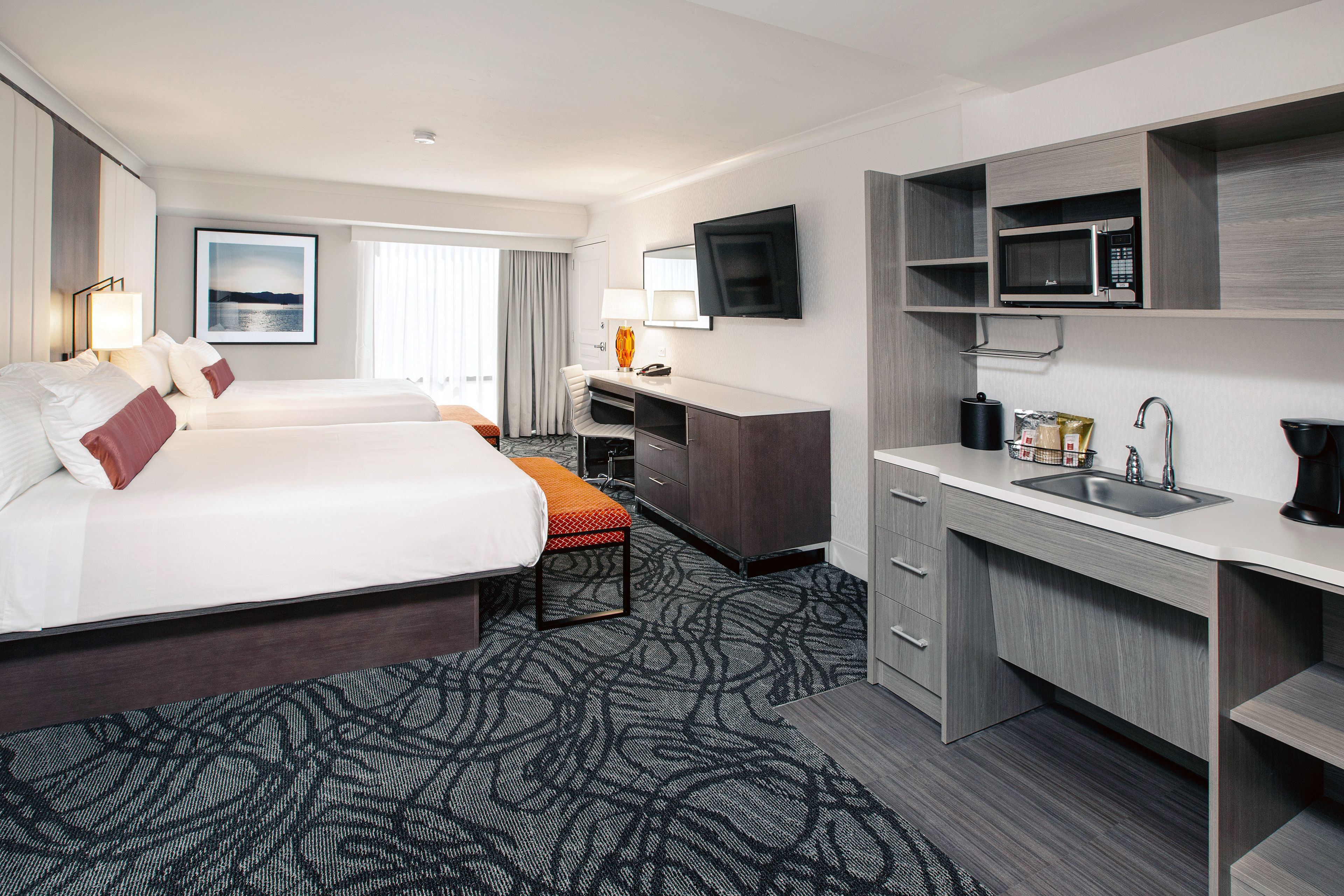 A hotel room with a large bed, a desk, a flat-screen TV, a microwave, and a sink.