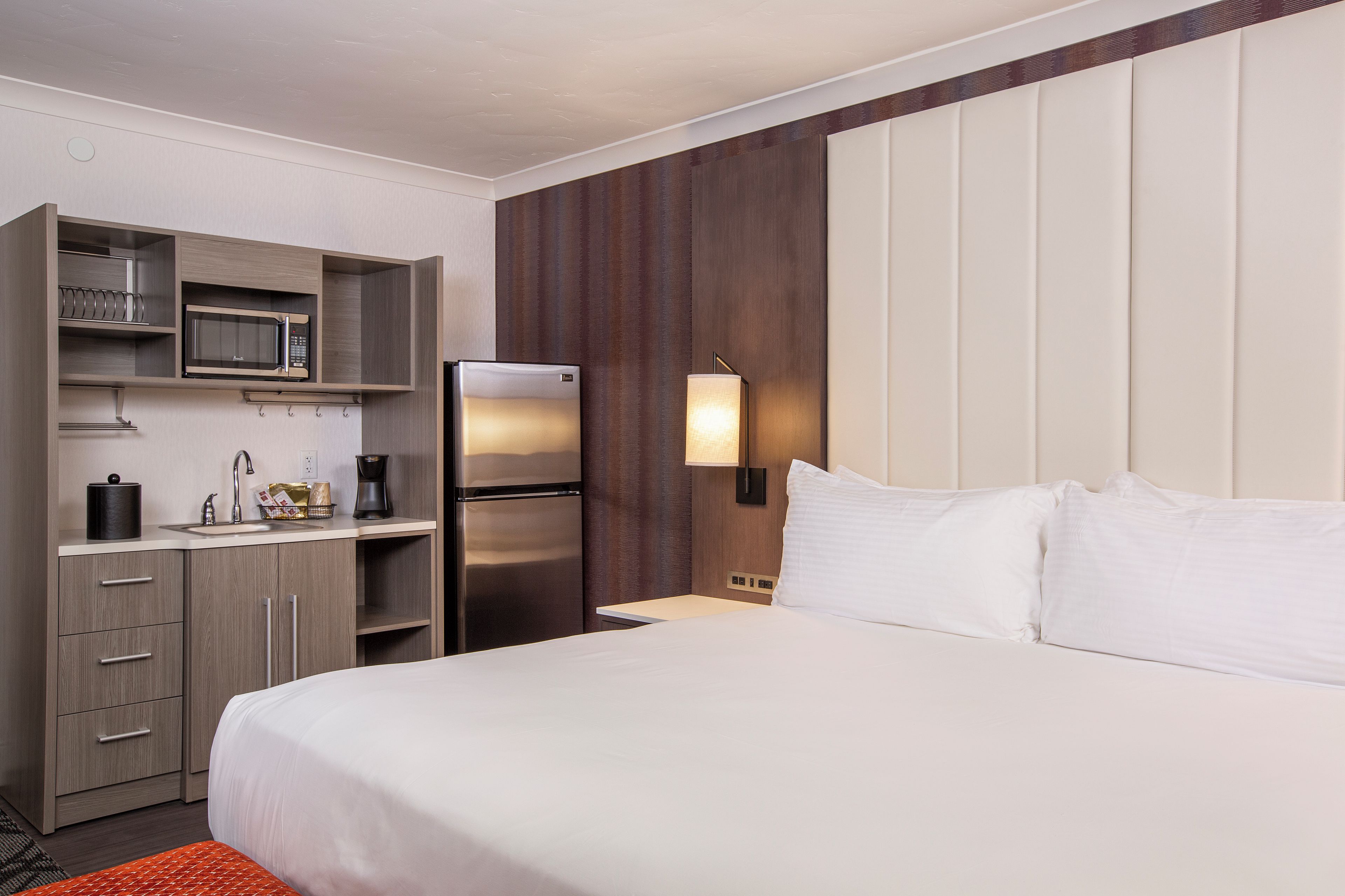 Een hotelkamer met een bed, een minibar, een koelkast, een magnetron en een wandlamp.