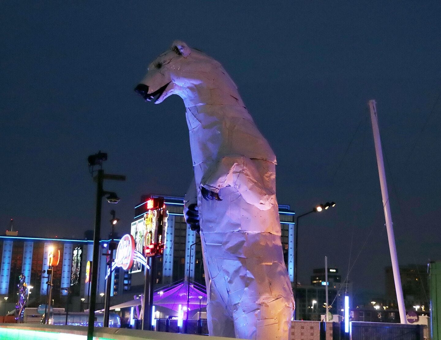 Uma grande estátua de urso polar branco em ambiente urbano à noite.