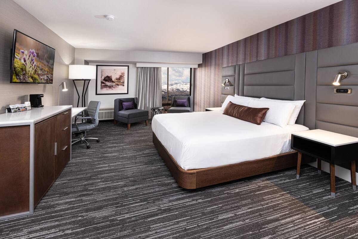 A hotel room with a large bed, a desk, a chair, a TV, and a view of the mountains.