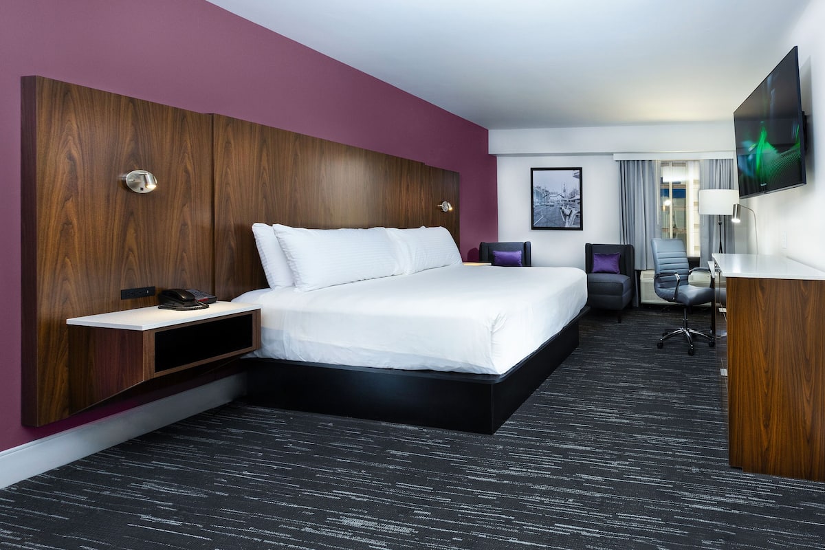 A modern hotel room with a large bed, a desk, and a TV.