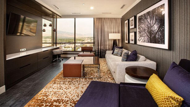 A modern hotel room with a large window, a flat-screen TV, a sofa, a coffee table, and a patterned rug. - J Resort (Reno)