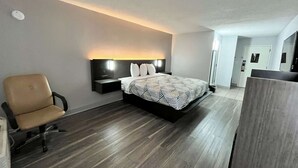 Una habitación de hotel moderna con cama, una silla, una mesita de noche y cabecero con iluminación integrada.