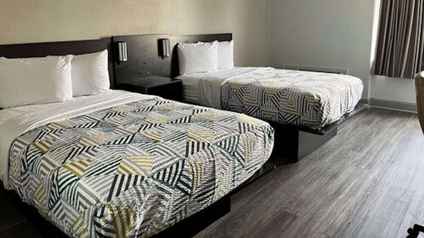 Habitación de hotel con dos camas, cada una con ropa de cama estampada, cabeceros de madera, mesitas de noche y una ventana con cortinas.