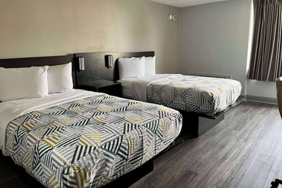 Habitación de hotel con dos camas, cada una con ropa de cama estampada, cabeceros de madera, mesitas de noche y un ventanal con cortinas.