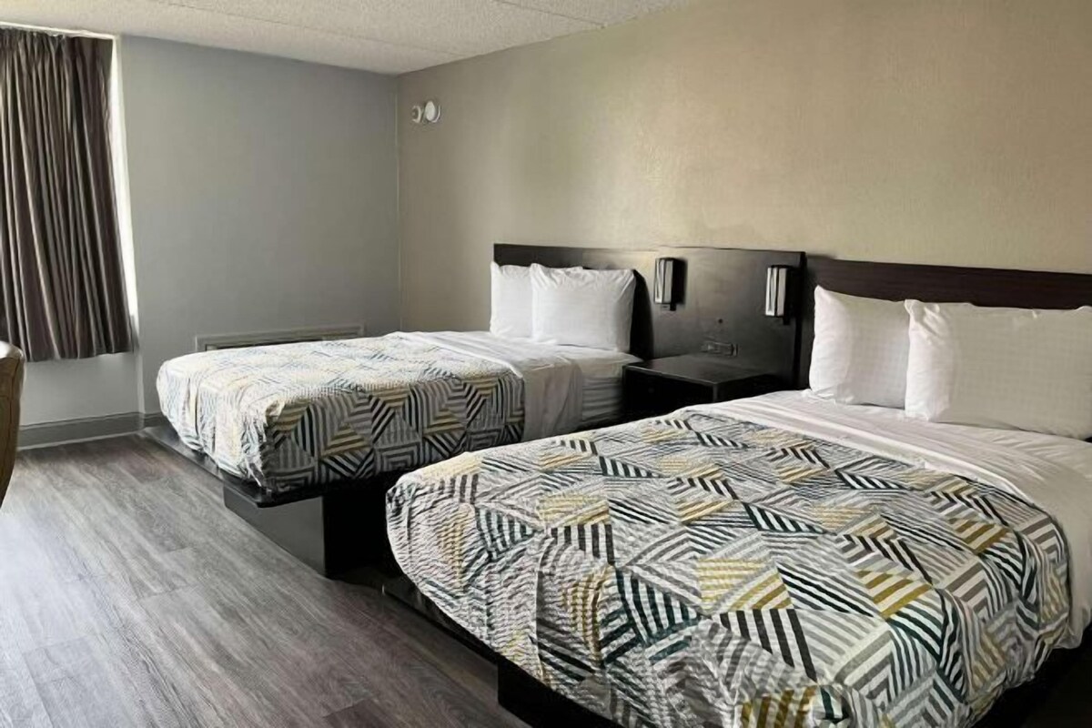 Quarto de hotel com duas camas, cada uma com colcha estampada, mesa de cabeceira e luminária fixada na parede.