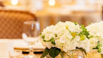 Une table à manger sur laquelle se trouve un vase en verre transparent contenant des fleurs blanches, une bougie allumée et un verre d’eau.