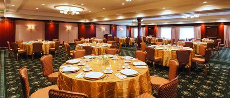 Une salle de banquet avec des tables rondes dressées pour le repas, équipées de chaises et de couverts.