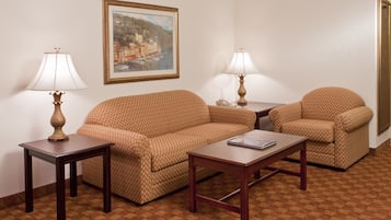 Une chambre d’hôtel avec un canapé à motifs, deux fauteuils assortis, une petite table, deux lampes et un tableau encadré accroché au mur.