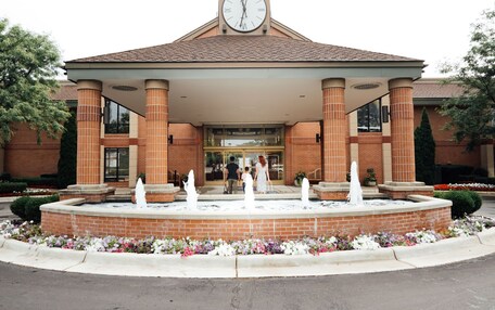 A hotel entrance with a clock, brick columns, and a fountain.