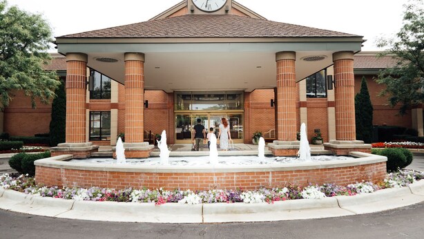 A hotel entrance with a clock, brick columns, and a fountain. - Ann Arbor Regent Hotel & Suites (Ann Arbor)
