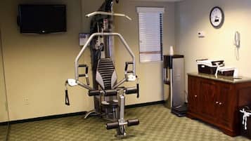A medical examination room with a patient lift, a cabinet, a clock, and a television on the wall.