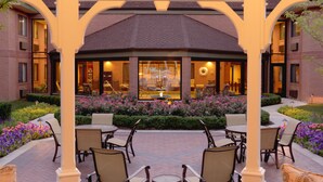 A covered outdoor seating area with brick walls and a central table, surrounded by chairs and potted plants. - Ann Arbor Regent Hotel & Suites (Ann Arbor)