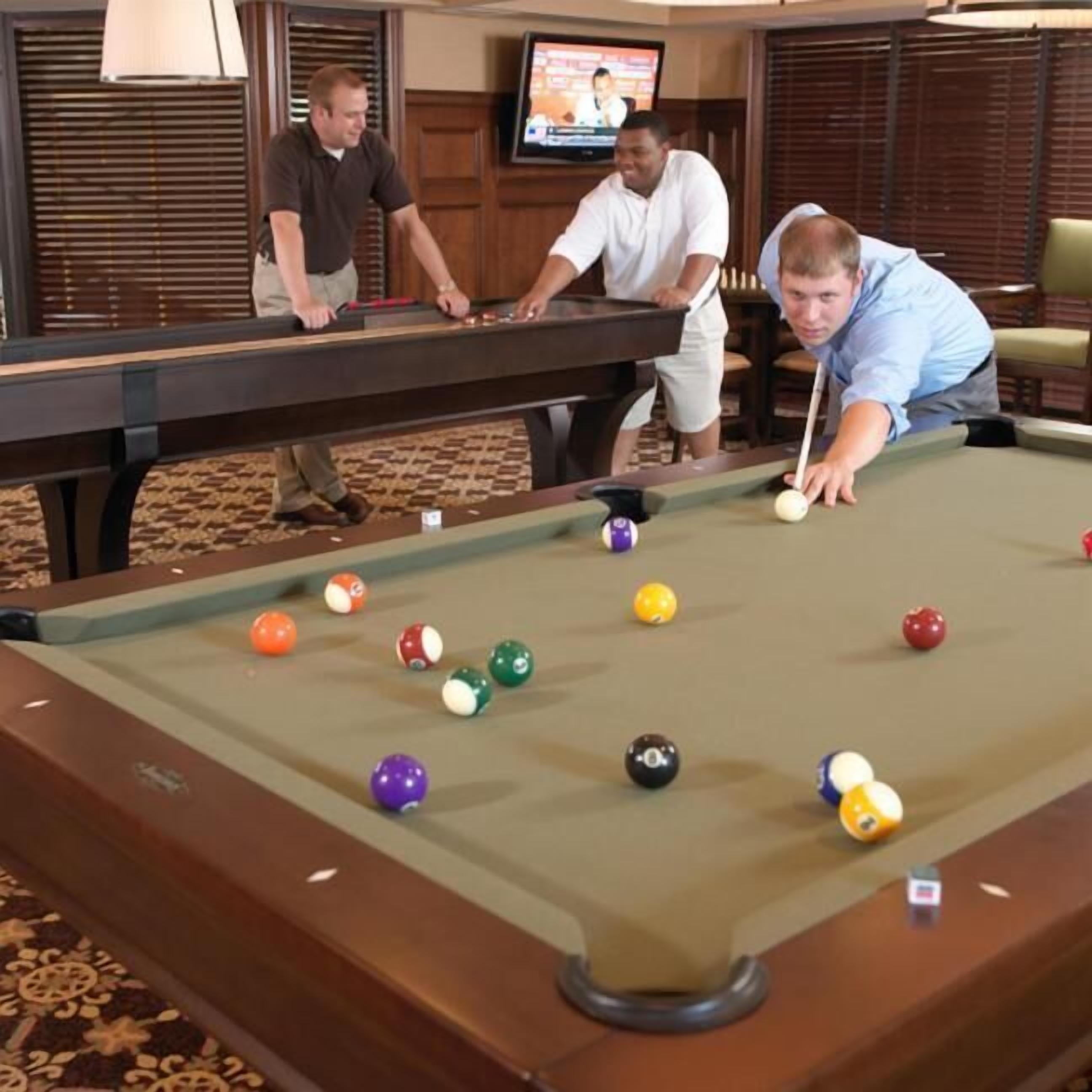 A pool table with several balls, a television in the background, and wooden paneling.