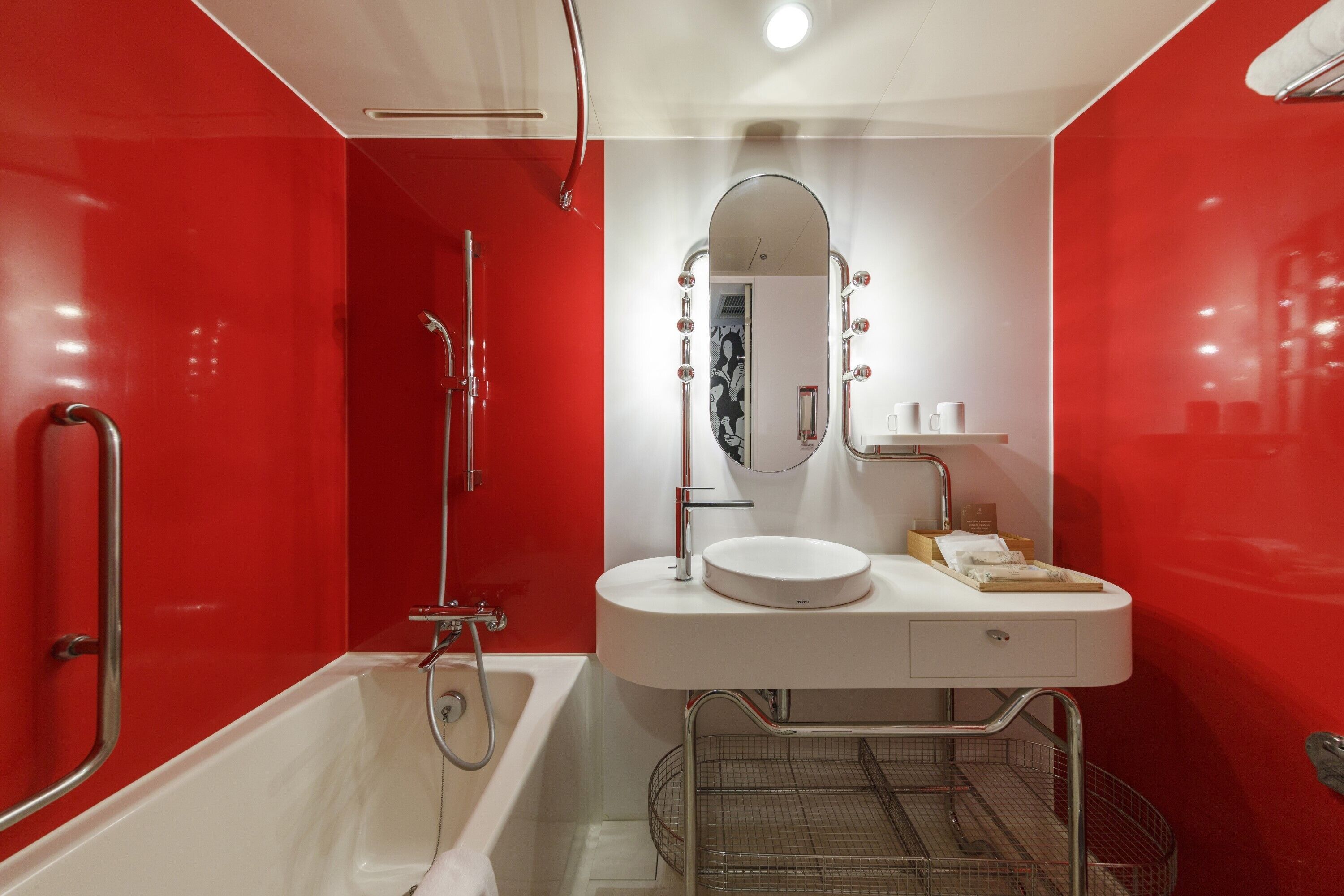 A modern bathroom with a red accent wall, a white sink, a mirror with lights, and a shower.