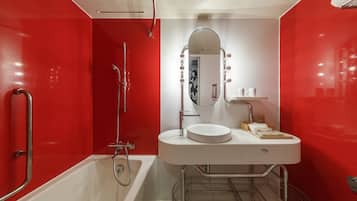 A modern bathroom with a red accent wall, a white sink, a mirror with lights, and a shower.