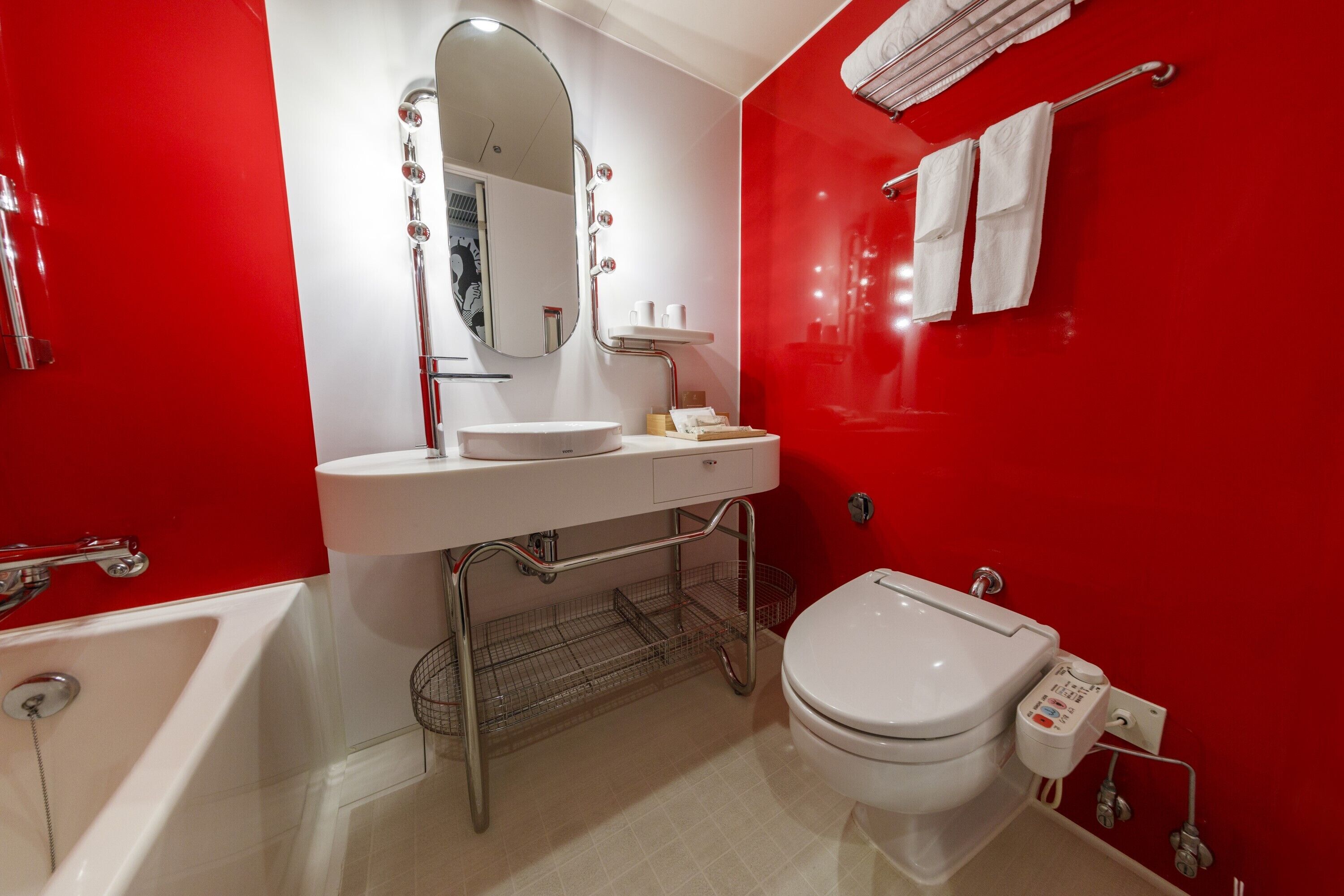 Une salle de bain moderne avec un mur d’accent rouge, un lavabo blanc, un miroir, des toilettes et une baignoire.