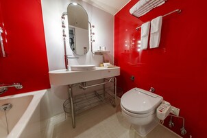 Un baño moderno con una pared de acento roja, un lavamanos blanco, un espejo, un inodoro y una bañera.