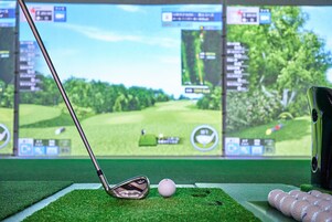Egy golfszimulátor, amely golfütőt, labdát és egy képernyőt tartalmaz, amelyen egy virtuális golfpálya látható.
