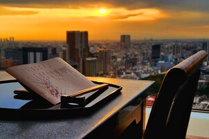 A table with a menu and chopsticks, overlooking a cityscape at sunset.