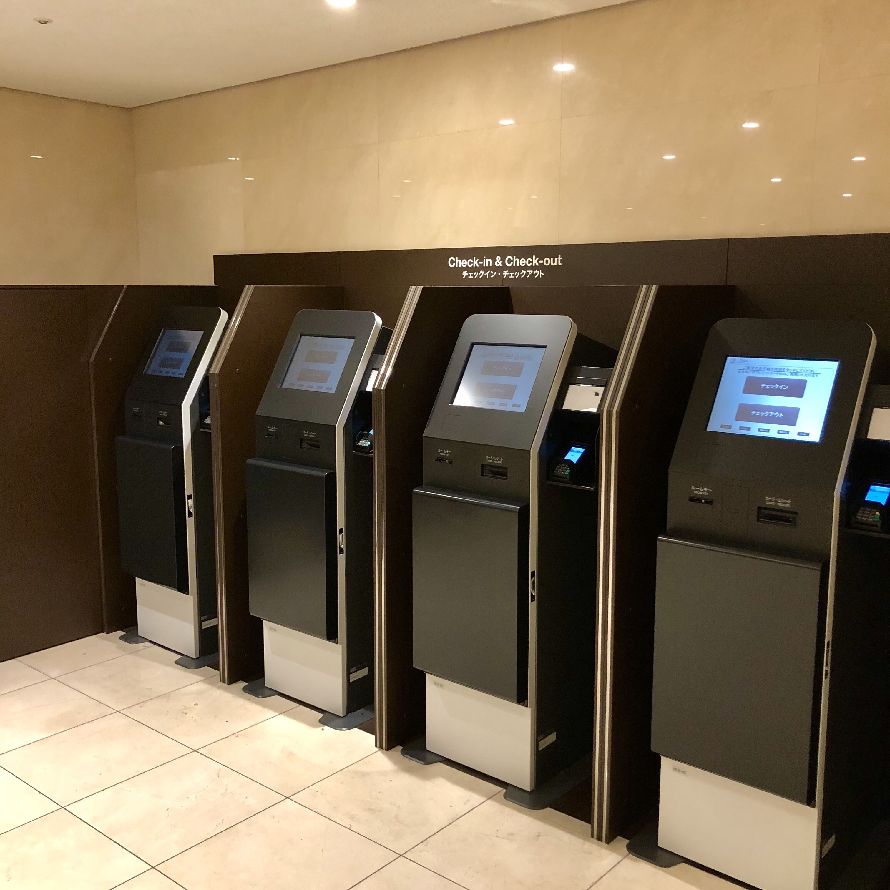 A row of check-in and check-out kiosks in a hotel lobby.