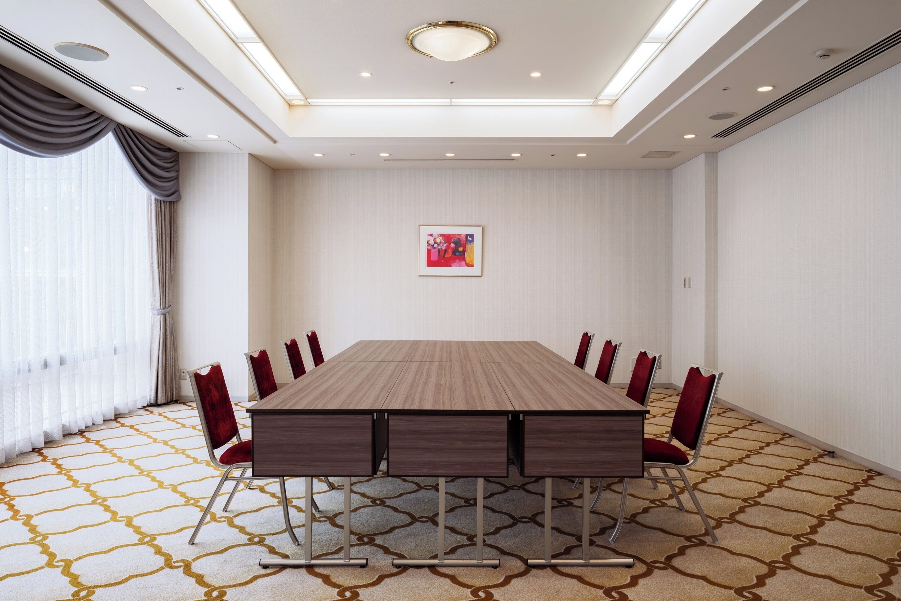 Ein Konferenzraum mit einem langen Tisch, roten Stühlen, einem gemusterten Teppich und einer Decke mit Einbaustrahlern.