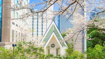 A building with a triangular roof and a green accent, surrounded by blooming trees.