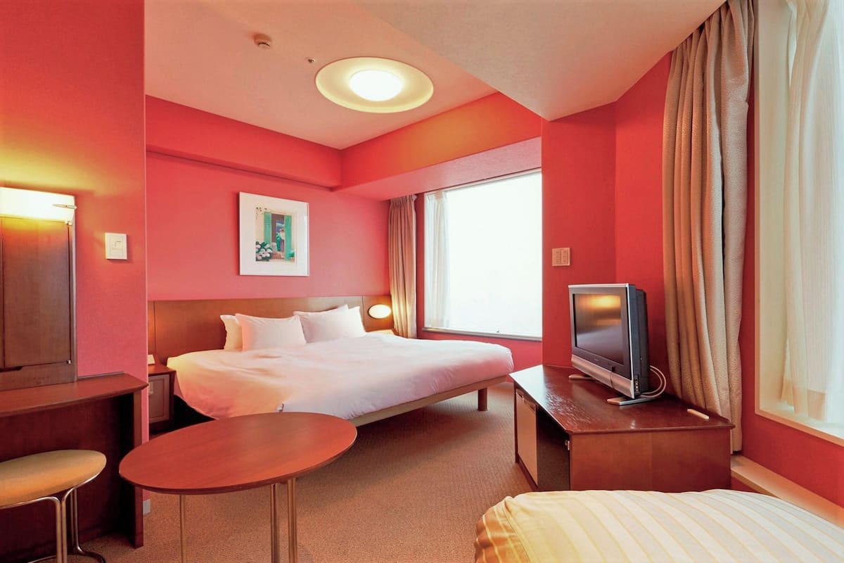 A hotel room with a bed, a TV, a desk, and a chair.