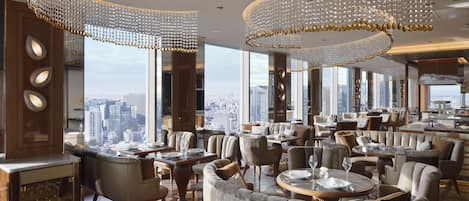 A spacious hotel lobby with high ceilings, elegant chandeliers, and a city view.