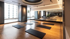 A spacious indoor area with wooden flooring and black mats arranged for exercise.